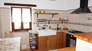 A kitchen with wooden cabinets, a sink, a stove, and a window with curtains. - Arriola Txiki Apartment - Andutz (Deba)