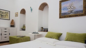 A neatly arranged bedroom with a bed, pillows, a small table, and decorative items including a ship painting and a seahorse.