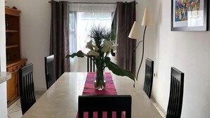 Comedor con una mesa blanca, sillas negras, un florero con flores blancas y un mantel individual rojo.