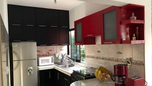 Una cocina con gabinetes negros, un microondas blanco, una cafetera roja y un frutero.