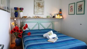 A neatly made bed with a blue striped bedspread, a vase with red flowers, and a small book on the bed. - Casa Papaveri e Conchiglie (Riccione)