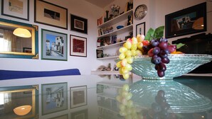 A room with a glass table reflecting the walls, a blue sofa, and a decorative bowl with grapes. - Casa Papaveri e Conchiglie (Riccione)