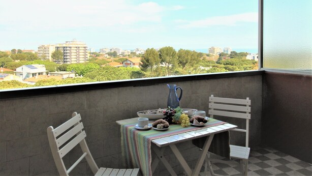 A balcony with a table set for breakfast, a chair, and a view of the cityscape. - Casa Papaveri e Conchiglie (Riccione)