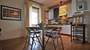 A modern kitchen with a dining table and chairs, a fruit bowl, and a birdcage on a cart. - Casa Papaveri e Conchiglie (Riccione)