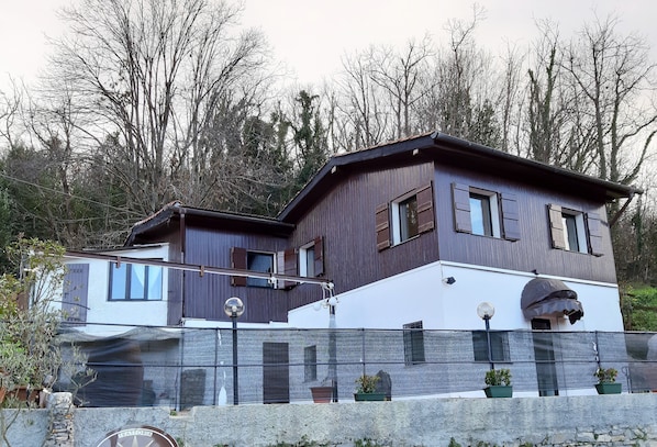 A modern two-story house with a stone foundation, a balcony with potted plants, and a satellite dish.