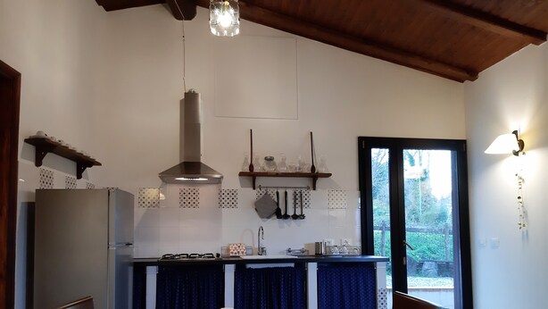 Una cocina con estufa, lavabo y utensilios colgando. Hay una mesa de comedor con sillas y una cesta de flores.
