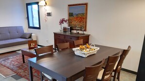 Un comedor con una mesa y sillas de madera, un florero con flores, un cuadro en la pared y un sofá al fondo.