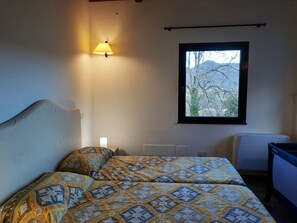 A bedroom with a bed, a bedside lamp, a window with a view of trees, and a radiator. - Casa La Violara (Santa Margherita Ligure)