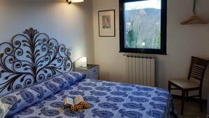 Un dormitorio con cama, mesita de noche, ventana con vista a árboles, radiador y una silla.