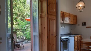 A kitchen with wooden cabinets, a stainless steel oven, and a dining area with a table and chairs. - Casa Isotta (Bonassola)