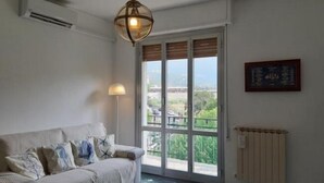 A living room with a sofa, a floor lamp, a large window with a view, and a radiator. - Welcome on Board (Levanto)
