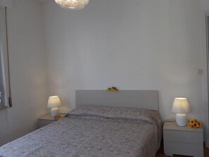 A bedroom with a bed, two bedside tables with lamps, a nightstand with a lamp and a flower, and a ceiling light fixture. - Welcome on Board (Levanto)