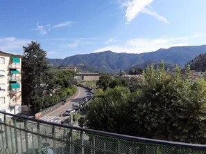 A residential area with a curved road, a pedestrian crossing, and a view of mountains in the background. - Welcome on Board (Levanto)