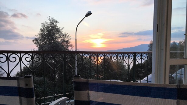 A balcony with striped chairs, a street lamp, and a sunset view.