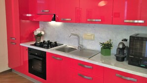 A modern kitchen with red cabinets, a black stove, a sink, and a coffee maker.