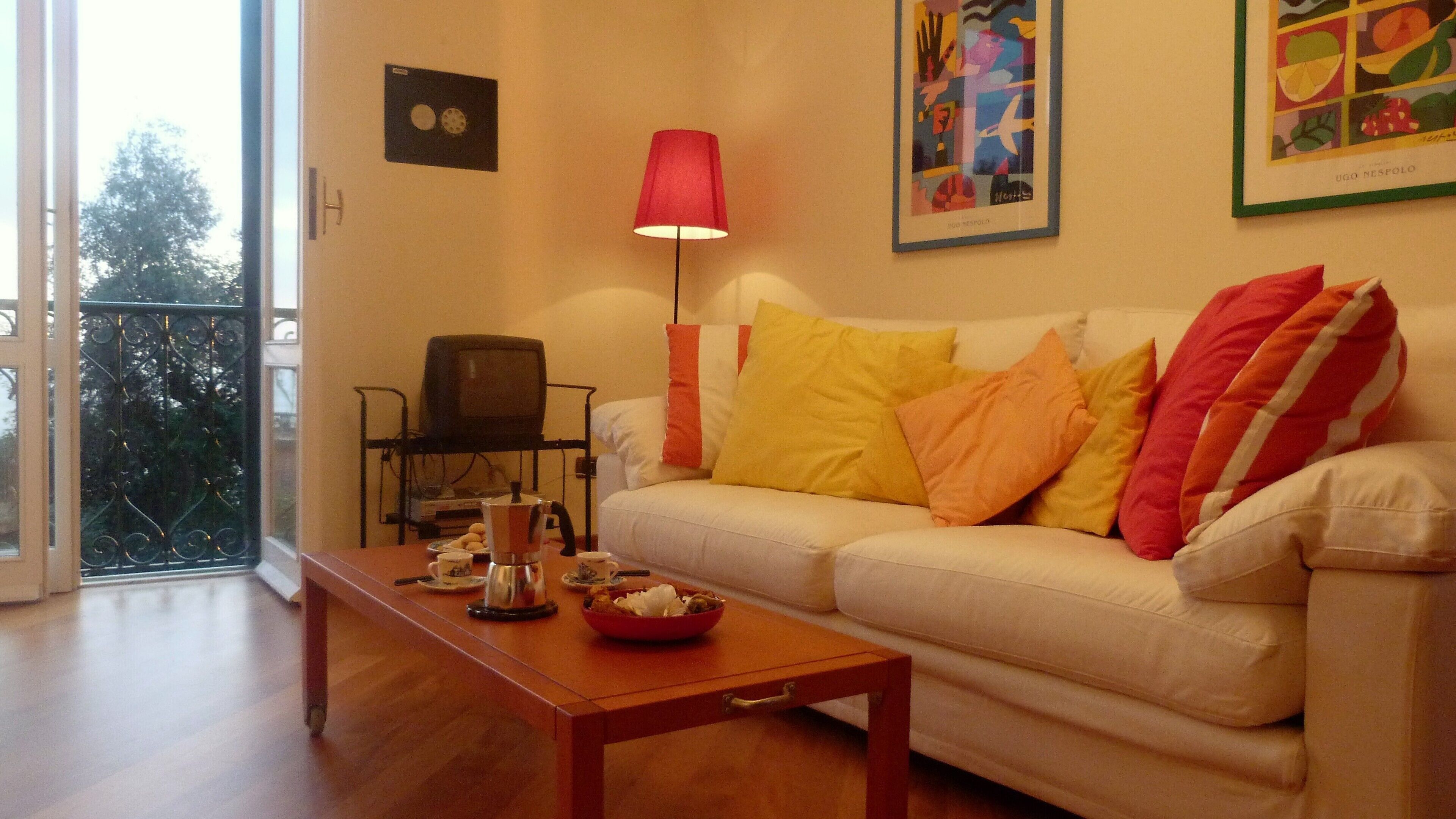 A living room with a sofa, a coffee table, a red lamp, and a painting on the wall.
