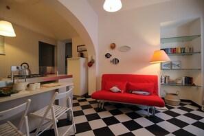 A compact living space with a kitchenette, a red sofa, a dining area with chairs, and a checkered floor.