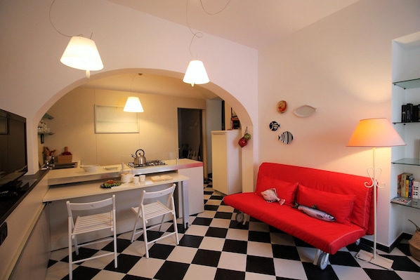 A compact living space with a kitchenette, a dining area, a red sofa, and a checkered floor.