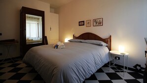 Uma cama bem arrumada com colcha listrada, uma mesa de cabeceira com abajur e um espelho na parede.