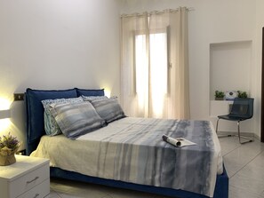 Ein Schlafzimmer mit einem Bett, einem Schreibtisch, einem Stuhl und einem Fenster mit Vorhängen.