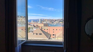 Une vue depuis une fenêtre donnant sur un paysage urbain, avec des bâtiments et une chaîne de montagnes lointaine.