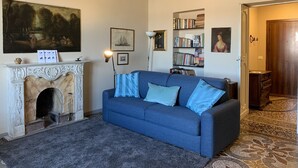 Un salon avec un canapé bleu, une cheminée, des étagères et un grand tableau accroché au mur.
