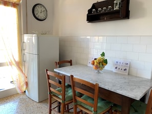 Una cocina con encimera de mármol, sillas de madera, un reloj y un frutero.