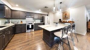 A modern kitchen with dark cabinets, stainless steel appliances, and a central island with bar stools. - Picturesque and Beautiful 3B on the Guadalupe River (New Braunfels)