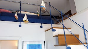 Habitación de varios niveles con literas, una escalera y un techo decorado con barcos de vela colgantes.
