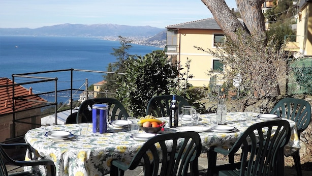 Un área de comedor al aire libre con una mesa preparada para cuatro, con vistas al mar y montañas a lo lejos.