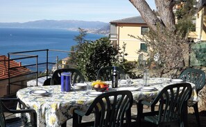 An outdoor dining area with a table set for four, overlooking a coastal view with mountains in the distance. - House Roby (Camogli)