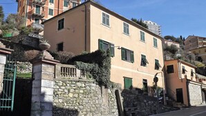 Un edificio de varios pisos con muros de piedra y contraventanas verdes, con balcones y un portón de piedra.