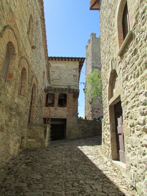 Eine enge Kopfsteinpflasterstraße, gesäumt von historischen Steinbauten mit Rundbogenfenstern, mit einem zentralen Gebäude, das einen Balkon besitzt.