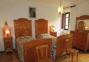 Un dormitorio con dos camas de madera, un aparador de madera, una silla, una mesita de noche con una lámpara y un candelabro colgante.