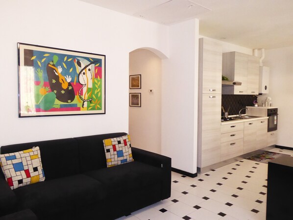 A modern living room with a black sofa, colorful cushions, and a vibrant abstract painting on the wall.