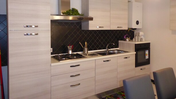 A modern kitchen with light wood cabinets, a black backsplash, stainless steel appliances, and a built-in oven. - Casa Ninni (Chiavari)