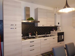 Cozinha moderna com armários de madeira clara, painel de fundo preto, eletrodomésticos de aço inoxidável e forno embutido.