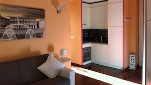 A modern living room with a sofa and a lamp, a kitchen with white cabinets, and a painting of a fountain on the wall. - House Nervi (Genoa)