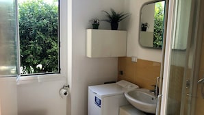 A compact bathroom with a toilet, a small sink, a mirror, and a window. - House Nervi (Genoa)