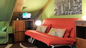 A small, cozy room with a sloped ceiling, a red sofa with cushions, a television on a wooden cabinet, and a cityscape painting on the wall. - Sotto la Mole (Turin)