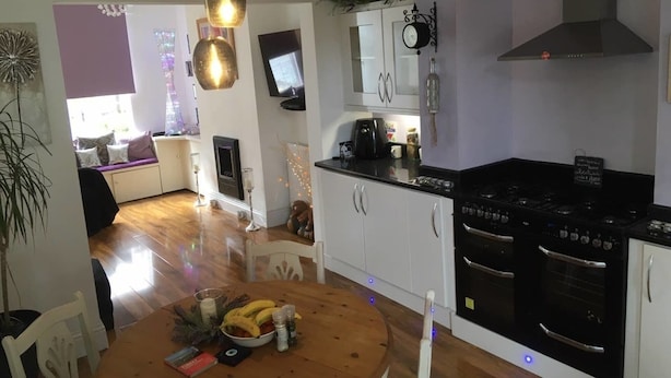 Uma cozinha moderna com armários brancos, fogão preto e área de jantar com mesa de madeira para dois.