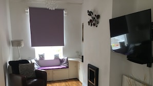 Uma sala de estar com sofá, televisão na parede, lareira e janela com persianas.