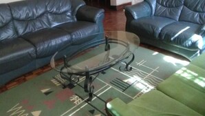 A living room with two black leather sofas, a glass coffee table, and a patterned rug. - Magline Conference And Guest House (Kisumu)