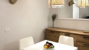 Ein Essbereich mit einem weißen Tisch, vier weißen Stühlen, einer Holzkabine und zwei wandmontierten Lampen mit Webmuster.