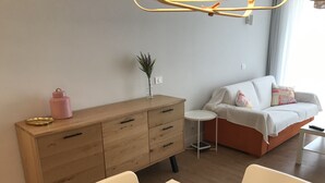 Ein modernes Wohnzimmer mit einem Holzschrank, einem weißen Tisch und einer Couch mit bunten Kissen.