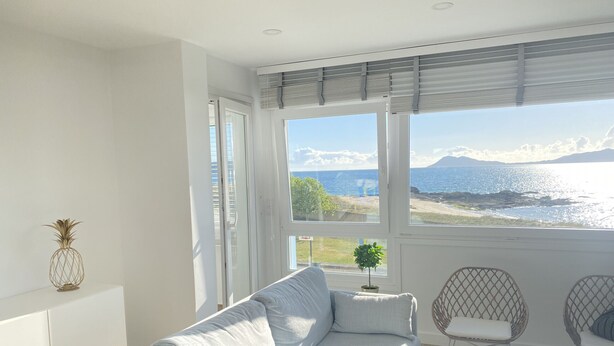 A modern living room with a sofa, a small table, and two wicker chairs. Large windows offer a view of the sea and mountains. - OH LA LIFE  PORTOSIN LA PLAYA Beachfront (Portosin)
