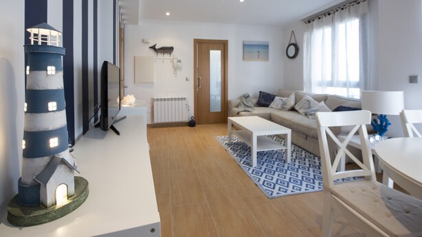 A modern living room with a white sofa, a coffee table, and a small dining table. There is a decorative lighthouse model and a wall-mounted telephone. - OH LA LIFE! PORTOSIN SAN JOSÉ (Portosin)