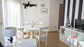 A dining area with a round table and white chairs, a white cabinet with a TV, and nautical-themed decor. - OH LA LIFE! PORTOSIN SAN JOSÉ (Portosin)