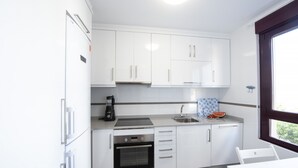 A modern kitchen with white cabinets, a built-in oven, a coffee maker, and a window providing natural light. - OH LA LIFE! PORTOSIN SAN JOSÉ (Portosin)