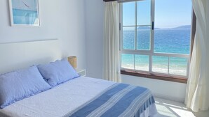 Un dormitorio con cama, ventana con cortinas, mesita de noche y un cuadro colgado en la pared.